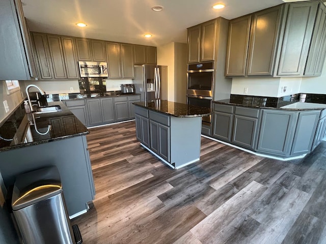 kitchen with a kitchen island, a sink, appliances with stainless steel finishes, dark wood-style floors, and dark stone countertops