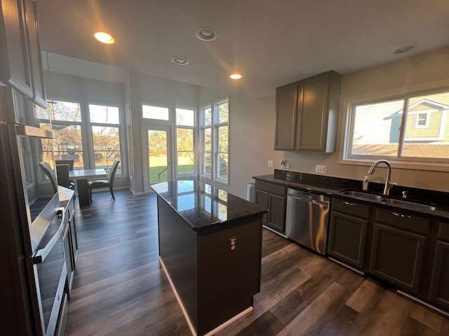 kitchen with dark wood-type flooring, a sink, stainless steel dishwasher, a center island, and dark stone counters