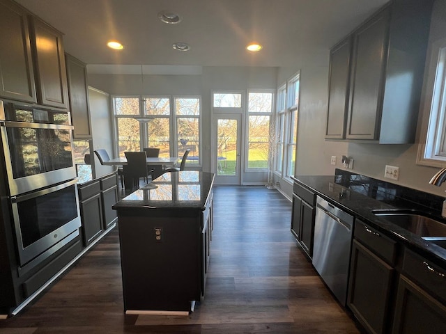 kitchen with stainless steel appliances, dark wood-type flooring, a sink, dark stone counters, and an island with sink