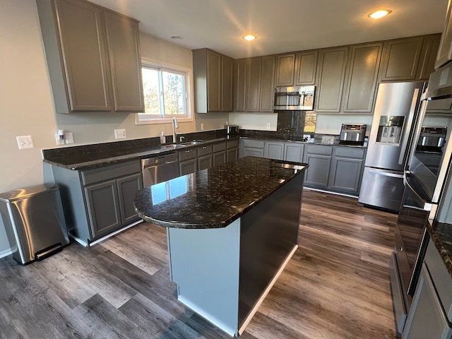 kitchen featuring a kitchen island, dark wood-type flooring, dark stone countertops, stainless steel appliances, and a sink