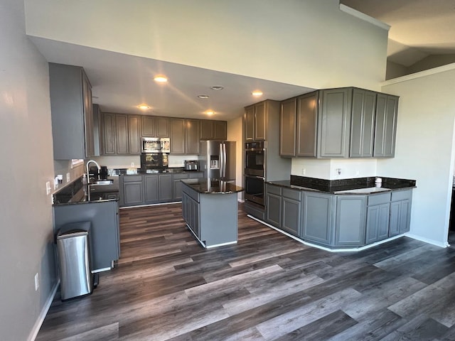 kitchen with appliances with stainless steel finishes, dark countertops, a center island, and a sink