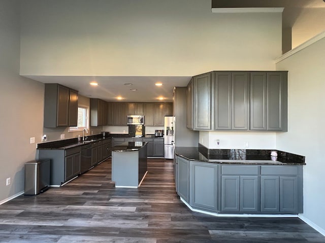 kitchen featuring stainless steel appliances, gray cabinetry, dark wood-type flooring, a kitchen island, and dark stone counters