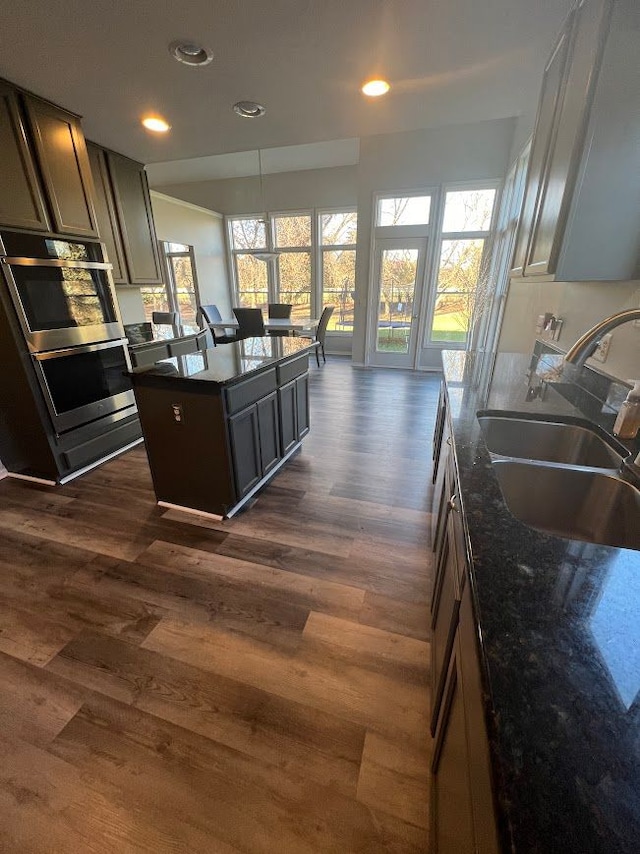 kitchen featuring dark wood finished floors, a center island, a sink, and dark stone countertops