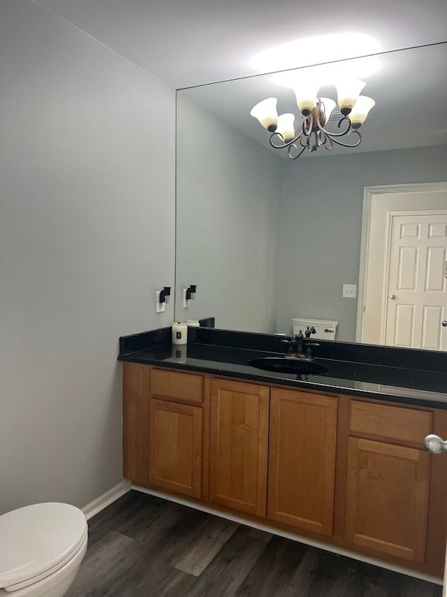 half bath featuring baseboards, toilet, wood finished floors, an inviting chandelier, and vanity