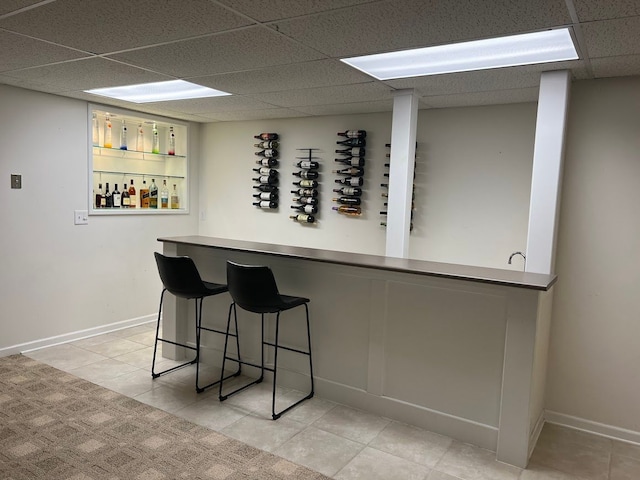 bar with baseboards, a drop ceiling, a dry bar, and light tile patterned floors