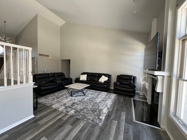 living room with a fireplace, high vaulted ceiling, visible vents, dark wood-type flooring, and a chandelier