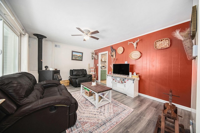 living room with ceiling fan, dark hardwood / wood-style flooring, a wood stove, and ornamental molding