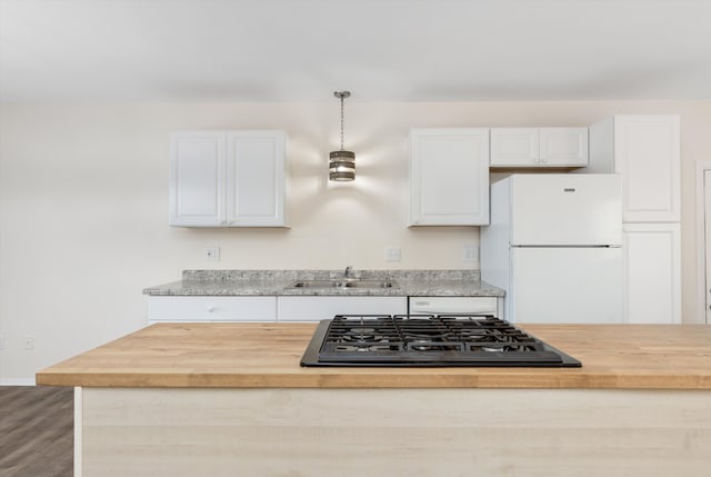 kitchen with stainless steel gas stovetop, hanging light fixtures, white cabinets, sink, and white refrigerator