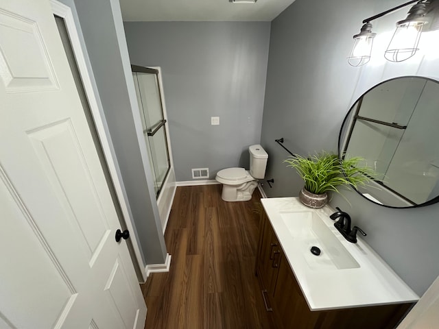 bathroom with wood-type flooring, toilet, vanity, and a shower with shower door