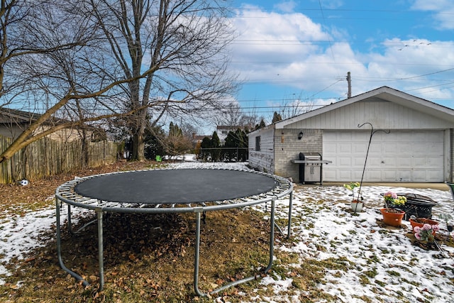 yard layered in snow with a garage and a trampoline