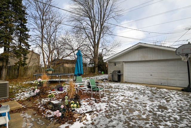 yard layered in snow with a garage, an outbuilding, cooling unit, and a trampoline