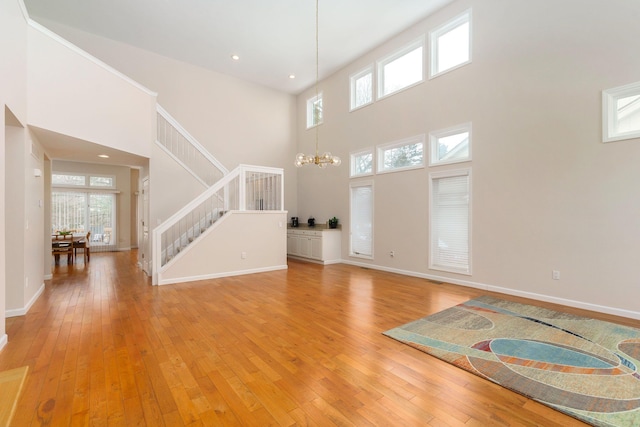 unfurnished living room with an inviting chandelier, light hardwood / wood-style flooring, and a high ceiling