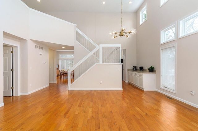 unfurnished living room with light hardwood / wood-style flooring, a towering ceiling, and an inviting chandelier