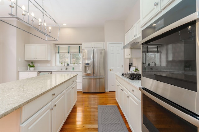 kitchen featuring white cabinets, decorative light fixtures, light hardwood / wood-style floors, and appliances with stainless steel finishes