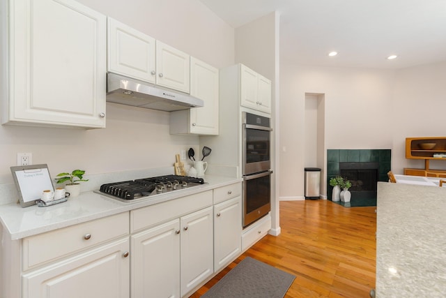 kitchen featuring white cabinets, a tile fireplace, stainless steel appliances, and light wood-type flooring