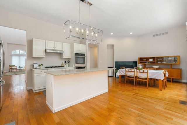 kitchen with a center island, white cabinetry, hanging light fixtures, and light hardwood / wood-style flooring