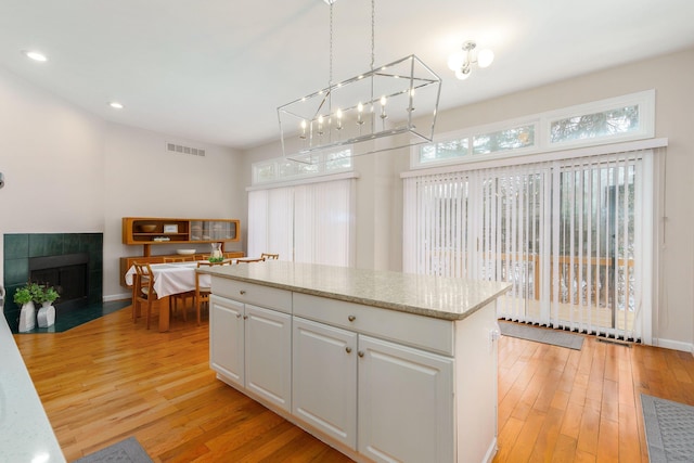 kitchen with hanging light fixtures, a tiled fireplace, light wood-type flooring, white cabinetry, and a center island