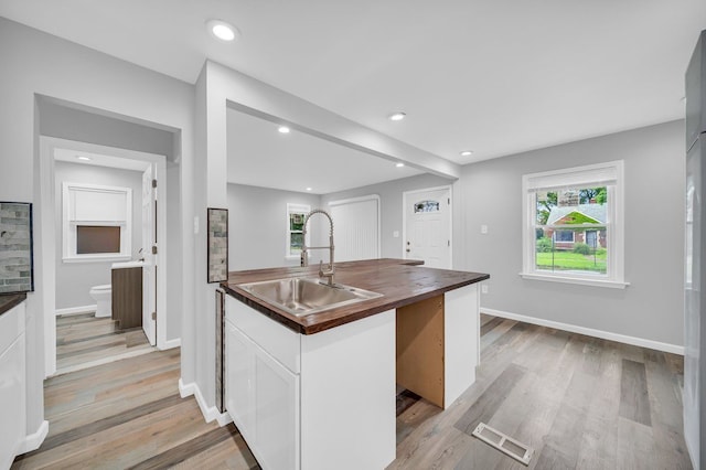 kitchen with butcher block counters, light hardwood / wood-style flooring, white cabinets, and sink