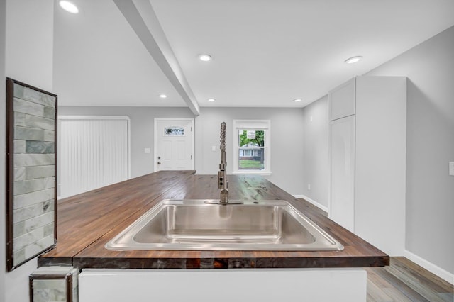 kitchen with light wood-type flooring, white cabinetry, butcher block countertops, and sink