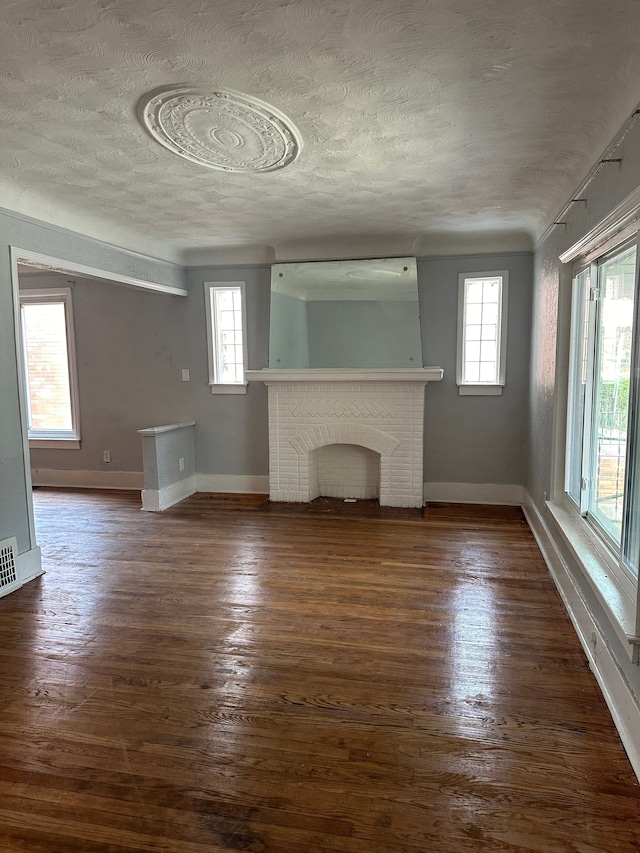 unfurnished living room with dark wood-type flooring, plenty of natural light, a textured ceiling, and a brick fireplace