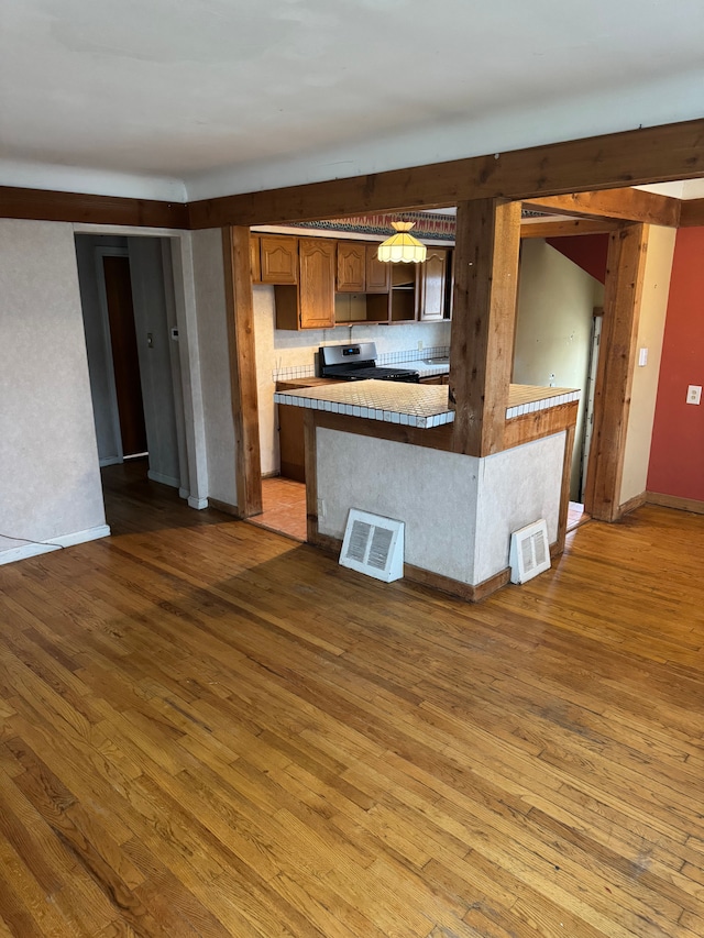 kitchen with decorative backsplash, kitchen peninsula, hardwood / wood-style floors, and stainless steel range oven