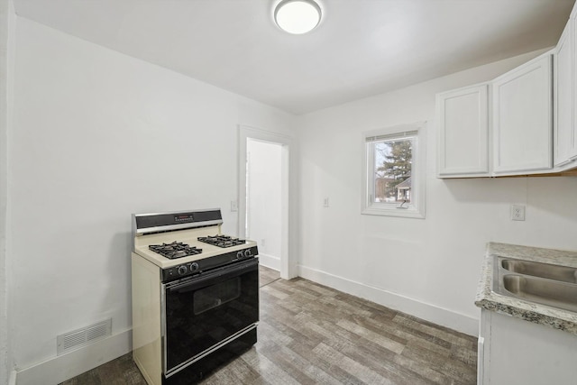 kitchen featuring sink, white cabinets, white gas range, and light hardwood / wood-style flooring