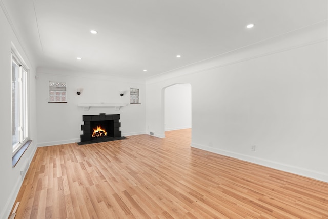 unfurnished living room with light wood-type flooring, a tiled fireplace, and ornamental molding