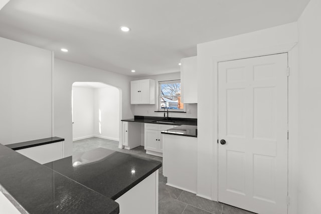 kitchen featuring white cabinets, kitchen peninsula, dark tile patterned flooring, and sink