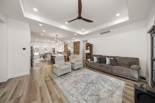 living room featuring ceiling fan with notable chandelier, light hardwood / wood-style flooring, and a tray ceiling