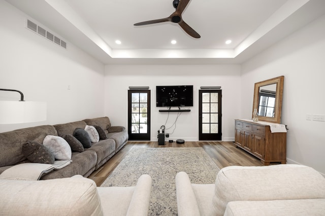 living room featuring a tray ceiling, ceiling fan, and wood-type flooring