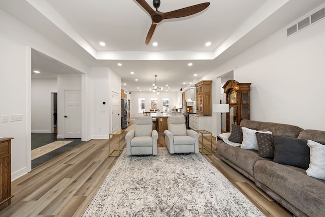 living room featuring ceiling fan with notable chandelier, hardwood / wood-style floors, and a tray ceiling