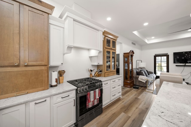 kitchen with white cabinetry, a raised ceiling, gas range, light stone counters, and light hardwood / wood-style flooring