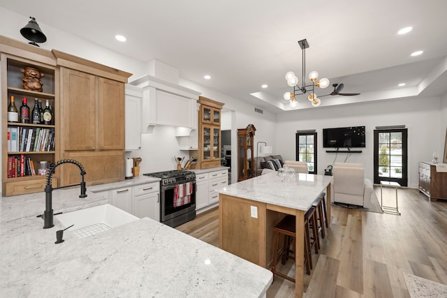 kitchen with a center island, gas stove, white cabinetry, sink, and a raised ceiling