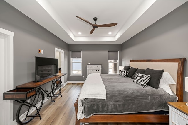 bedroom featuring light wood-type flooring, ceiling fan, and a raised ceiling