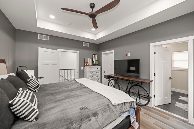 bedroom with ceiling fan, a raised ceiling, light hardwood / wood-style flooring, and access to outside