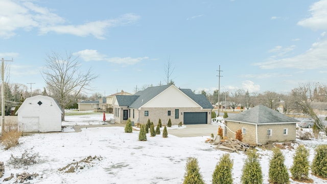 snow covered rear of property with a garage and a storage shed