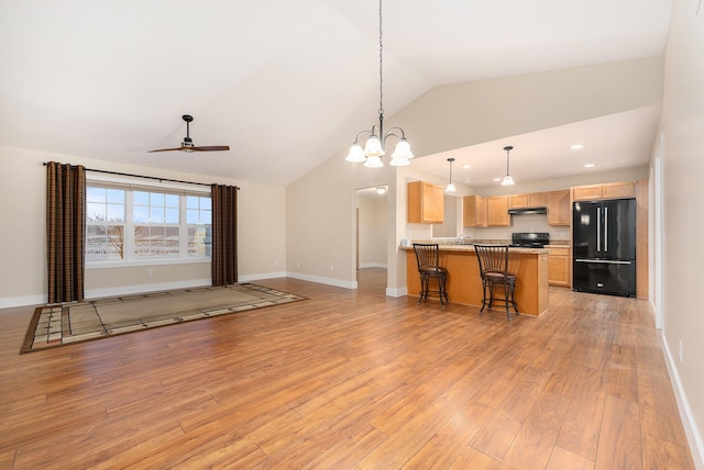 kitchen featuring black refrigerator, stove, lofted ceiling, light brown cabinetry, and pendant lighting