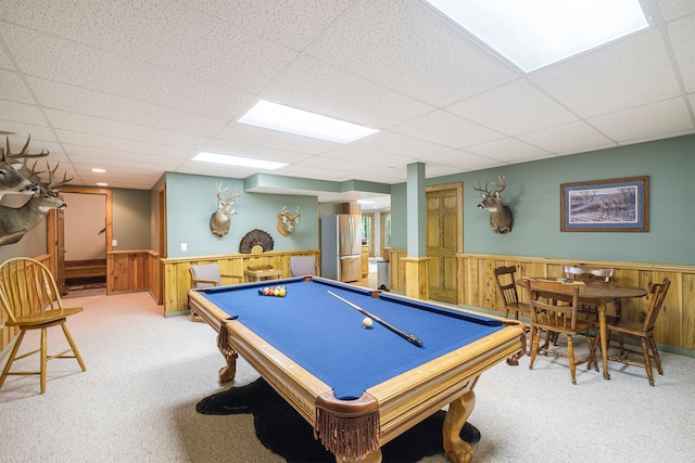 game room with a paneled ceiling, light carpet, and wooden walls