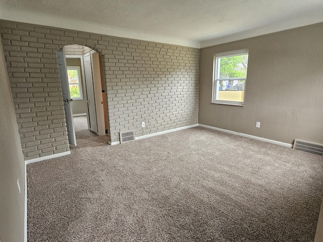 spare room with carpet, brick wall, and a textured ceiling