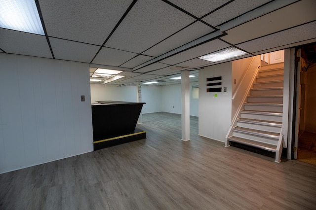 basement with a paneled ceiling, hardwood / wood-style floors, and bar area