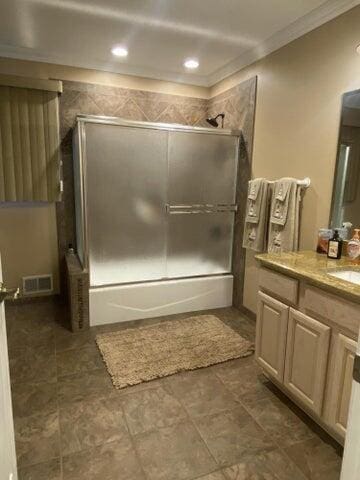 bathroom with bath / shower combo with glass door, vanity, and ornamental molding