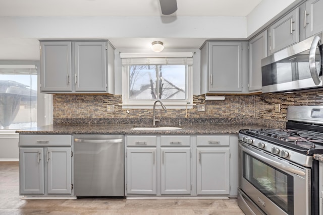 kitchen featuring gray cabinets, sink, light wood-type flooring, stainless steel appliances, and dark stone counters