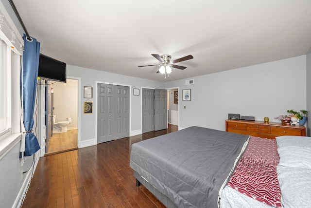 bedroom featuring ceiling fan, dark wood-type flooring, ensuite bathroom, and two closets