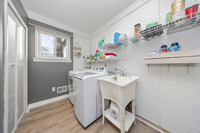 washroom featuring washer and dryer, light hardwood / wood-style floors, and brick wall