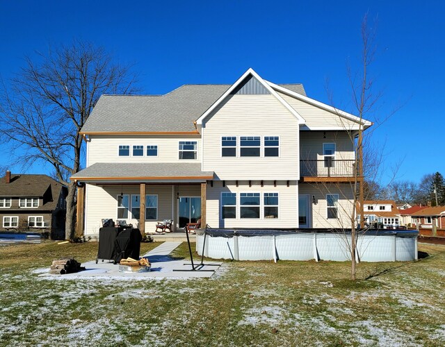 snow covered rear of property featuring a lawn, a covered pool, a patio, and a fire pit