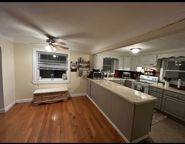 kitchen featuring dark wood-style flooring, white electric range oven, stainless steel microwave, gray cabinetry, and a peninsula