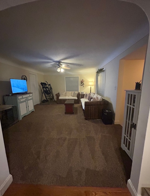 living area with ceiling fan, arched walkways, and dark colored carpet