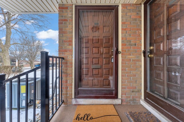 snow covered property entrance with a balcony and central AC