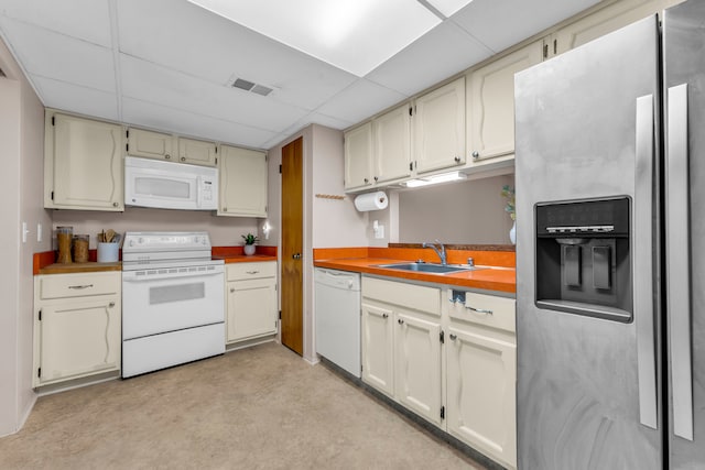 kitchen featuring sink, white appliances, cream cabinetry, and a drop ceiling