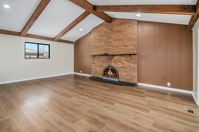 unfurnished living room with vaulted ceiling with beams, light wood-type flooring, a brick fireplace, and wooden walls